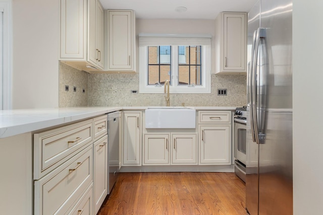 kitchen with appliances with stainless steel finishes, sink, light wood-type flooring, and decorative backsplash