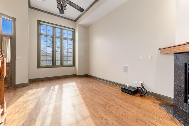 unfurnished living room with light hardwood / wood-style floors, ornamental molding, a premium fireplace, and ceiling fan