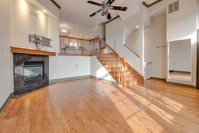 unfurnished living room featuring a towering ceiling, a premium fireplace, ceiling fan, and light wood-type flooring