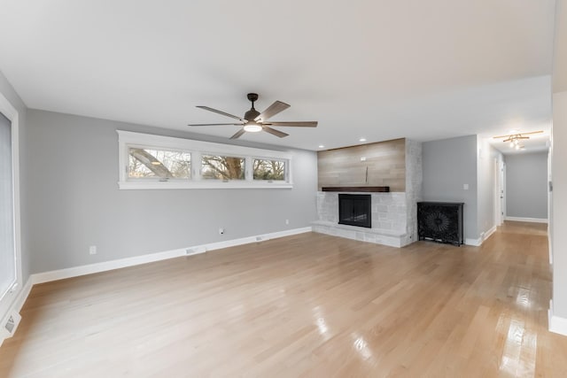 unfurnished living room featuring a large fireplace, ceiling fan, and light wood-type flooring