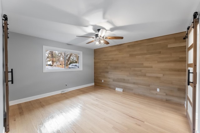 spare room with ceiling fan, wooden walls, a barn door, and light hardwood / wood-style floors