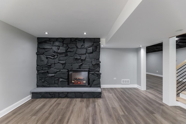 unfurnished living room with wood-type flooring and a stone fireplace