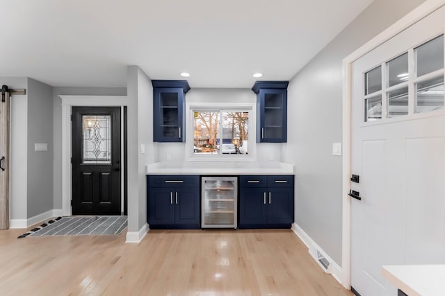 bar with blue cabinets, a barn door, beverage cooler, and light hardwood / wood-style flooring