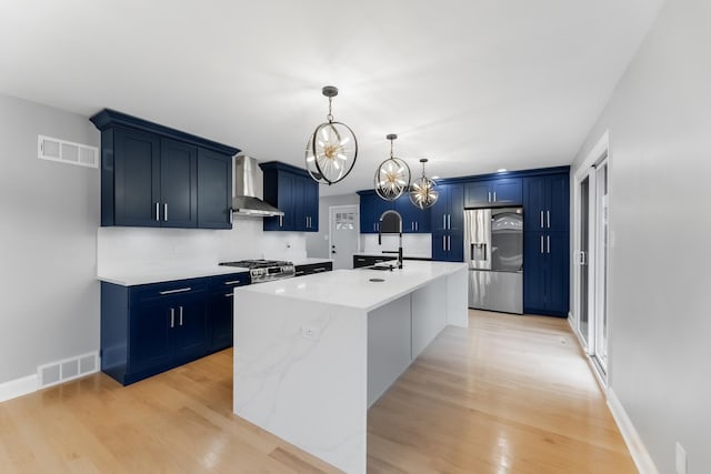 kitchen with sink, stainless steel appliances, wall chimney exhaust hood, and blue cabinetry