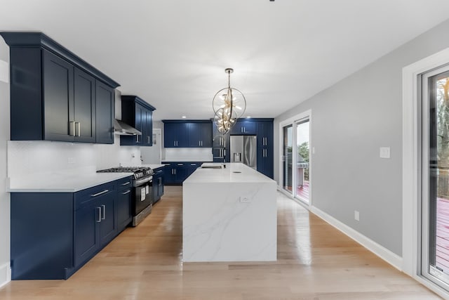 kitchen with an inviting chandelier, hanging light fixtures, stainless steel appliances, an island with sink, and light wood-type flooring