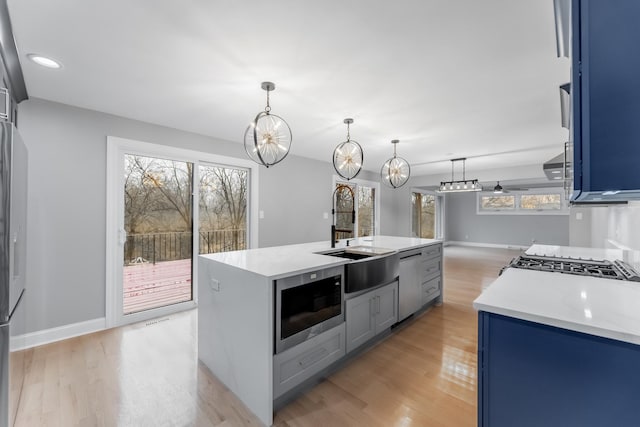 kitchen with stainless steel appliances, a kitchen island with sink, sink, and light wood-type flooring