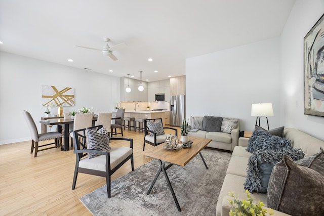 living room with ceiling fan, sink, and light wood-type flooring