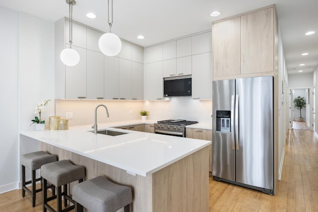 kitchen featuring sink, appliances with stainless steel finishes, decorative backsplash, decorative light fixtures, and light wood-type flooring