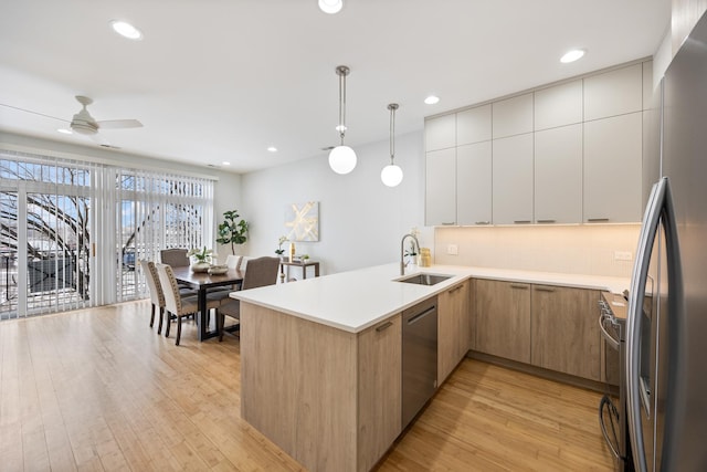 kitchen featuring sink, hanging light fixtures, kitchen peninsula, stainless steel appliances, and light hardwood / wood-style floors