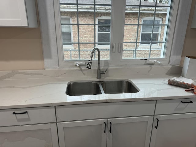 kitchen featuring light stone counters, sink, and white cabinets