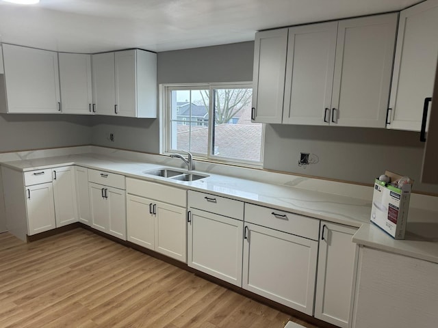 kitchen featuring light stone counters, sink, white cabinets, and light wood-type flooring