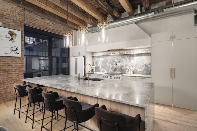 kitchen featuring sink, high end fridge, white cabinets, brick wall, and decorative light fixtures