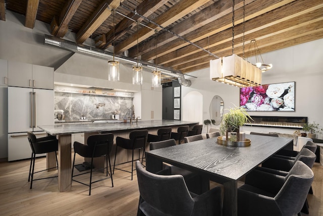 dining space with indoor bar, light wood-type flooring, and beam ceiling