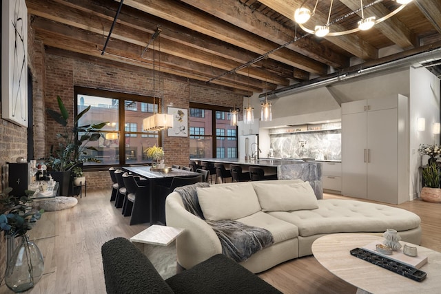 living room with brick wall, a towering ceiling, beam ceiling, and light hardwood / wood-style flooring