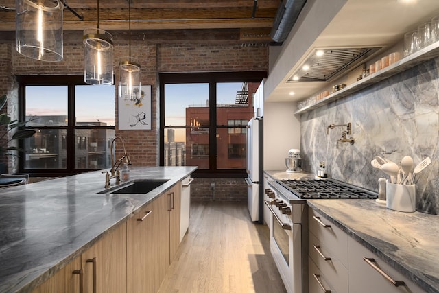 kitchen with stainless steel appliances, sink, decorative light fixtures, light hardwood / wood-style flooring, and brick wall