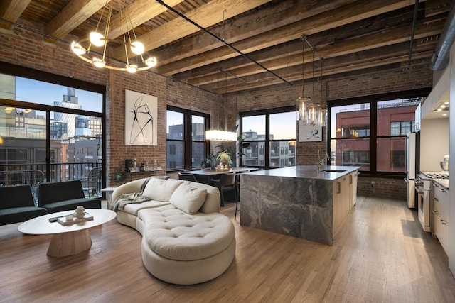 living room featuring brick wall, beam ceiling, a chandelier, and sink