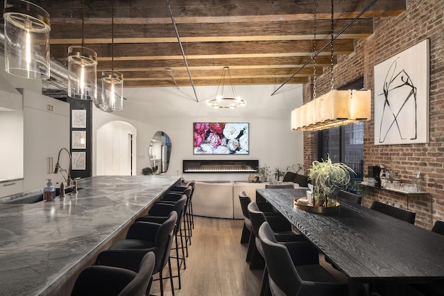 kitchen with hardwood / wood-style floors, brick wall, a breakfast bar area, and beam ceiling