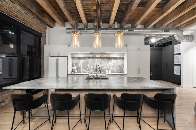 kitchen featuring sink, high end fridge, brick wall, white cabinets, and stone countertops