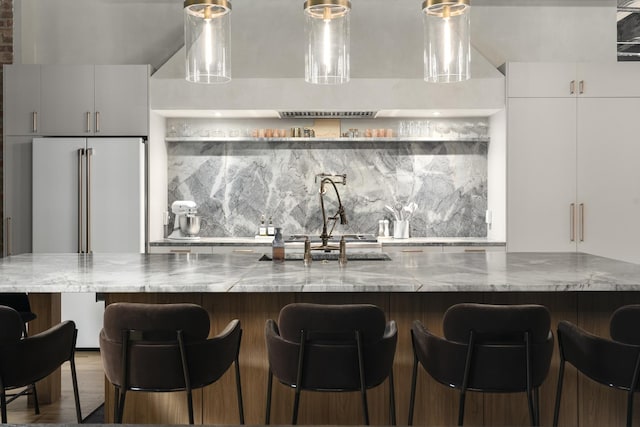 kitchen featuring a spacious island, high end fridge, a breakfast bar area, white cabinetry, and backsplash