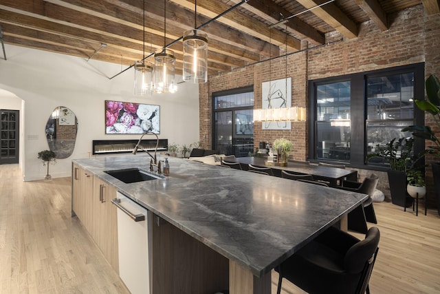 kitchen with sink, beam ceiling, dishwasher, and a center island with sink