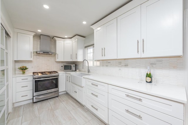 kitchen with wall chimney range hood, sink, appliances with stainless steel finishes, white cabinetry, and tasteful backsplash