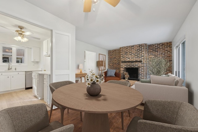 dining room with brick wall, sink, ceiling fan, a brick fireplace, and light hardwood / wood-style flooring