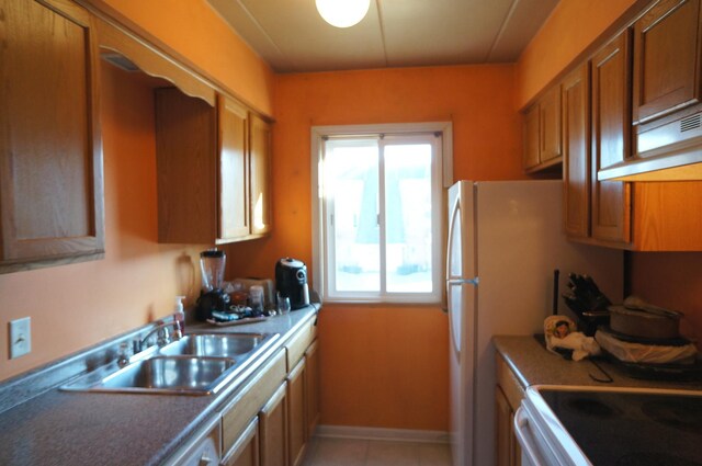 kitchen featuring light tile patterned flooring, brown cabinets, baseboards, and a sink