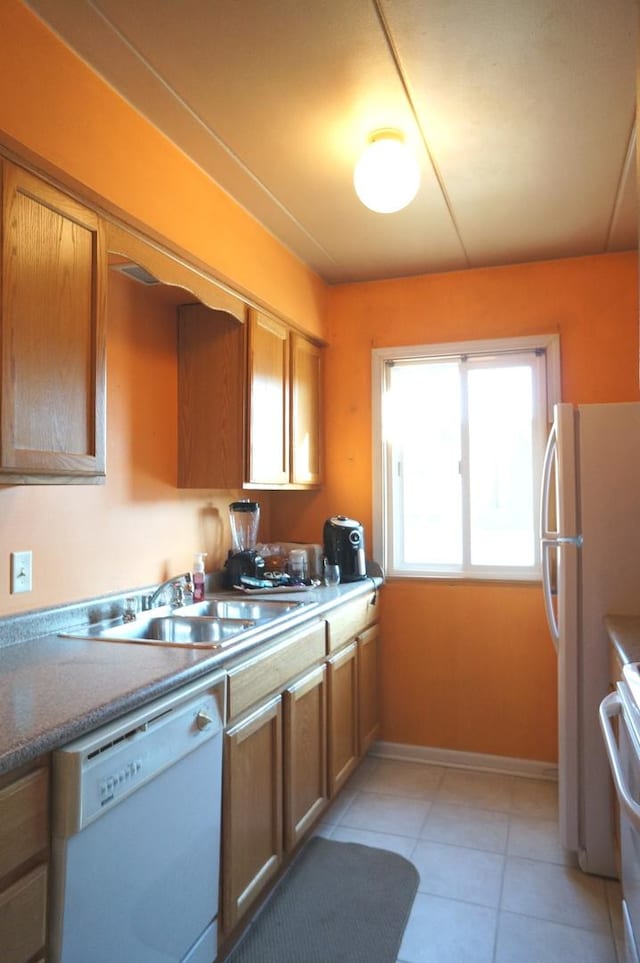 kitchen featuring baseboards, brown cabinets, light tile patterned flooring, white appliances, and a sink