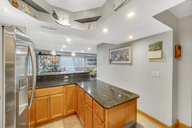 kitchen with light tile patterned floors, kitchen peninsula, dark stone counters, and stainless steel fridge with ice dispenser