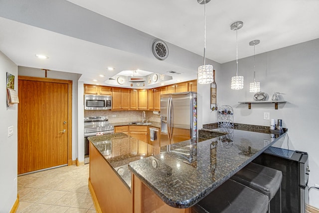 kitchen featuring appliances with stainless steel finishes, tasteful backsplash, dark stone countertops, a kitchen bar, and hanging light fixtures