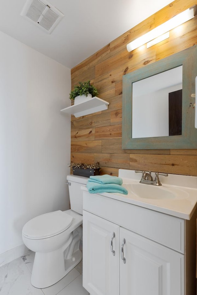 bathroom featuring vanity, wooden walls, and toilet