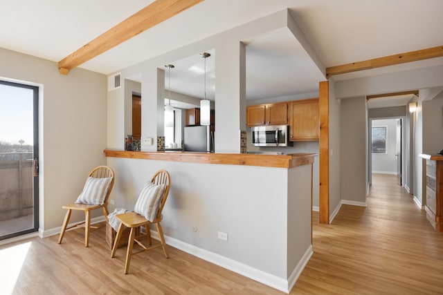 kitchen with appliances with stainless steel finishes, decorative light fixtures, light hardwood / wood-style floors, and kitchen peninsula