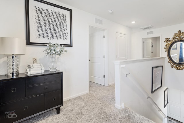 corridor with an upstairs landing, baseboards, visible vents, and light colored carpet