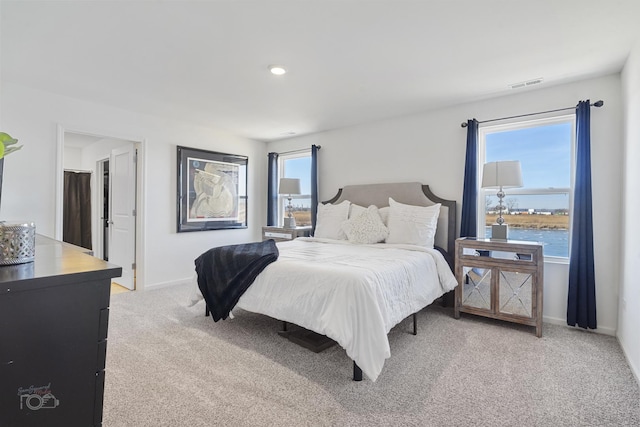 carpeted bedroom with a water view, visible vents, and baseboards