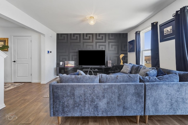 living area featuring dark wood-style floors, an accent wall, and baseboards