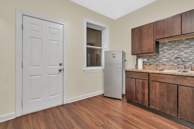 kitchen with sink, dark wood-type flooring, stainless steel refrigerator, tasteful backsplash, and dark brown cabinetry