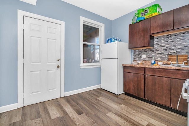 kitchen featuring dark brown cabinetry, backsplash, light hardwood / wood-style flooring, and white fridge