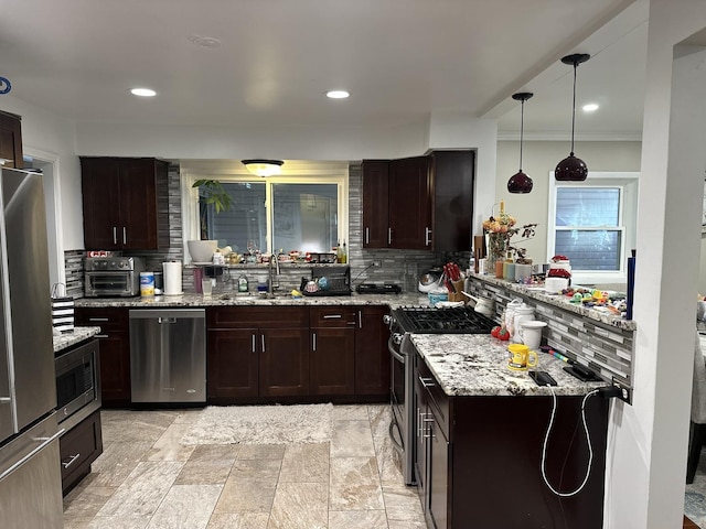 kitchen with appliances with stainless steel finishes, sink, backsplash, hanging light fixtures, and light stone countertops