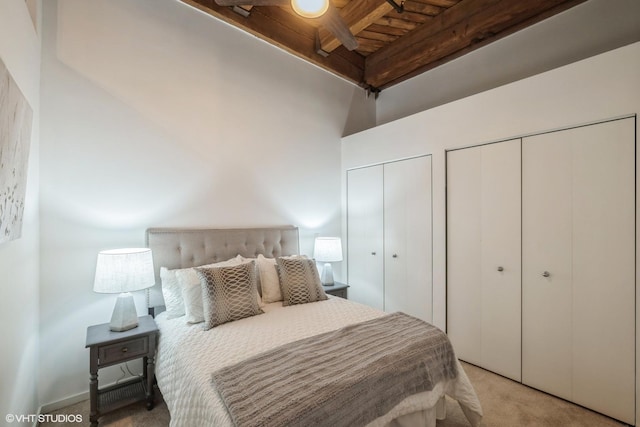 carpeted bedroom with two closets, beam ceiling, and wooden ceiling