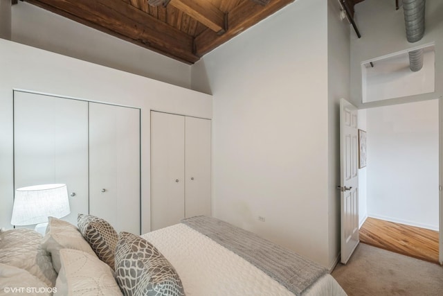 carpeted bedroom with wood ceiling, multiple closets, and beamed ceiling