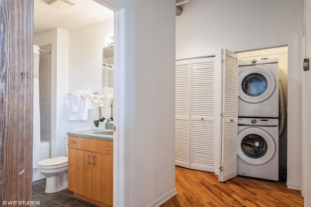 laundry room featuring sink, dark wood-type flooring, and stacked washer and clothes dryer