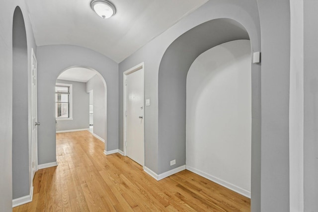 corridor with vaulted ceiling and light wood-type flooring