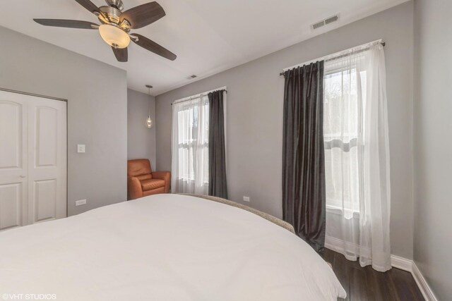 bedroom featuring multiple windows, dark wood-type flooring, ceiling fan, and a closet