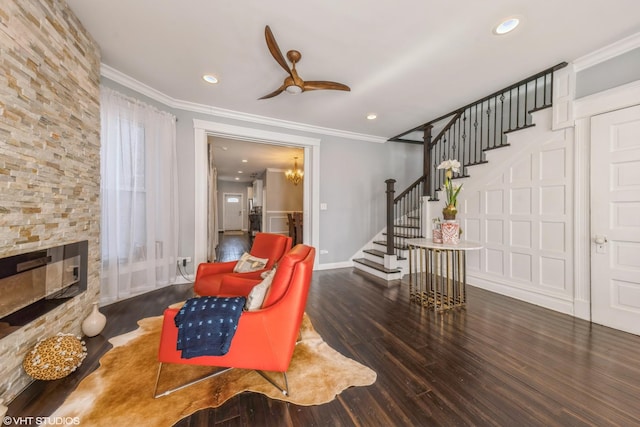 sitting room featuring a fireplace, crown molding, dark wood-type flooring, and ceiling fan with notable chandelier