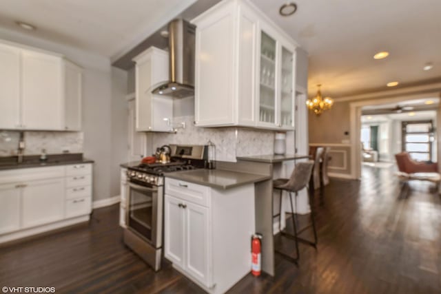 kitchen featuring white cabinets, stainless steel range with gas cooktop, a breakfast bar area, and wall chimney range hood