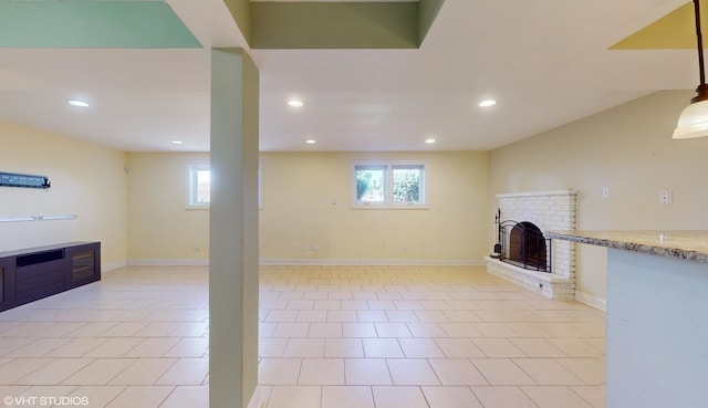 basement featuring a brick fireplace, plenty of natural light, and light tile patterned floors