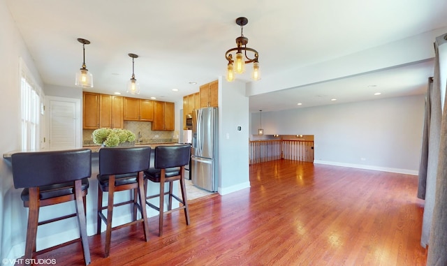 kitchen featuring wood-type flooring, decorative light fixtures, decorative backsplash, and stainless steel fridge with ice dispenser