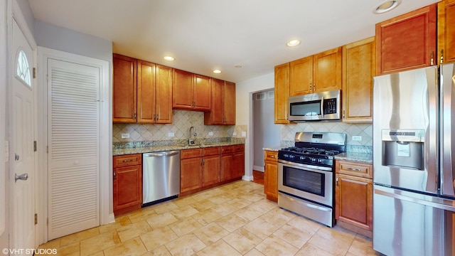 kitchen with light stone counters, appliances with stainless steel finishes, sink, and tasteful backsplash