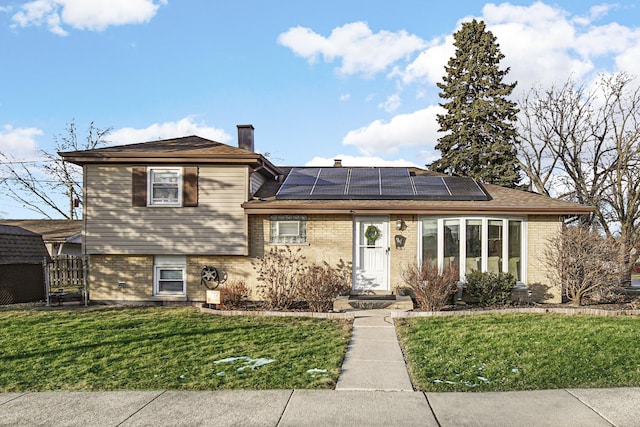 tri-level home with a front lawn and solar panels