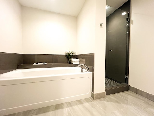 bathroom featuring a garden tub, a shower stall, and baseboards